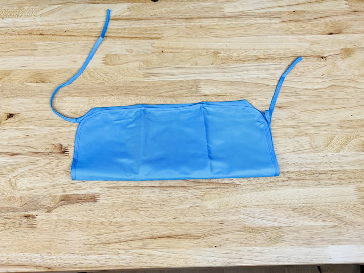 Here's a handy hack for you. Head over to Dollar Tree and snag one of their aprons. Begin by cutting off the neckties, then fold the top part underneath and the bottom part up. Take out your trusty hot glue gun and secure the sides and sections to craft pockets with this apron.