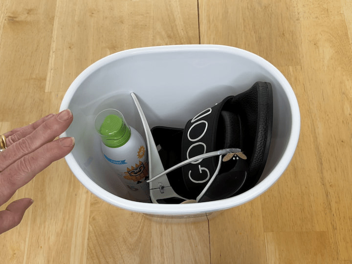 Let's go ahead and bring the bucket back and then I'm going to place the shoes in the bucket. I'm also going to place the sunglasses in the bucket and you could get a sunglasses case if you prefer and then my sunscreen.