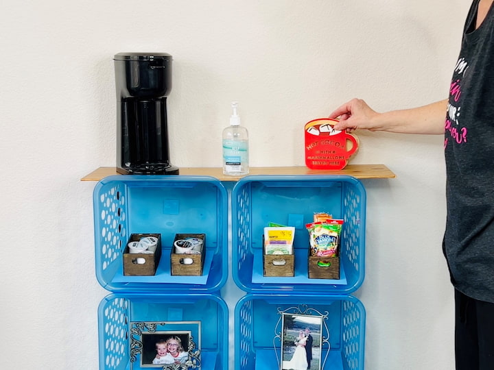 Now it's time to decorate. If you want to use these for closed storage you can buy some bins, baskets, or soft cloth crates to slide in to create drawers. I started by adding some books and frames on the bottom. I also added some snacks and coffee pods with a small coffee pot on top. I also added some hand sanitizer and a cute little hot chocolate. sign. You could also add a glass vase or flower pot.