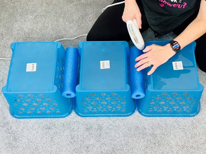 Next, grab your hot glue gun. I'm using my Xyron self-loading glue gun, which is super awesome, to hot glue each of the pool noodles into place between each of the baskets. This helps make them more stable. I repeated the process and made two sets of baskets.