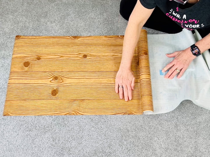 I grabbed some wood grain style contact paper from Dollar Tree to cover the poster board.  I measured the contact paper for the size of the poster board and I cut a little extra.  I peeled the backing off as I went and placed the contact paper onto the poster board, smoothing it out as I went to get rid of any bubbles.   